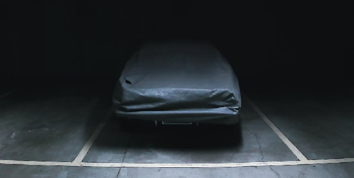 Classic car stored under a cover in a dark garage, awaiting its pre-season check